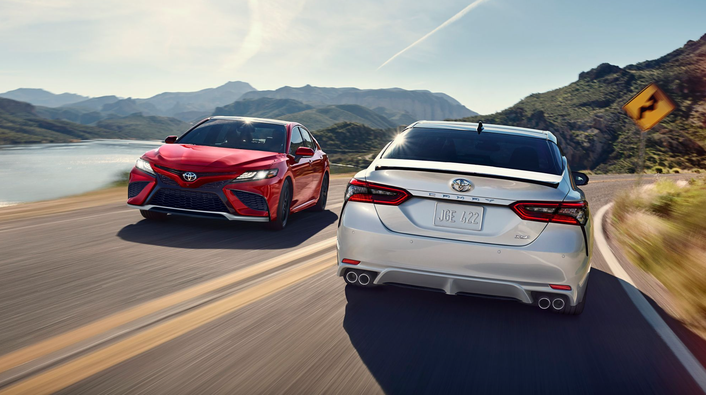 Two 2024 Toyota Camrys driving past each other with mountains in the background