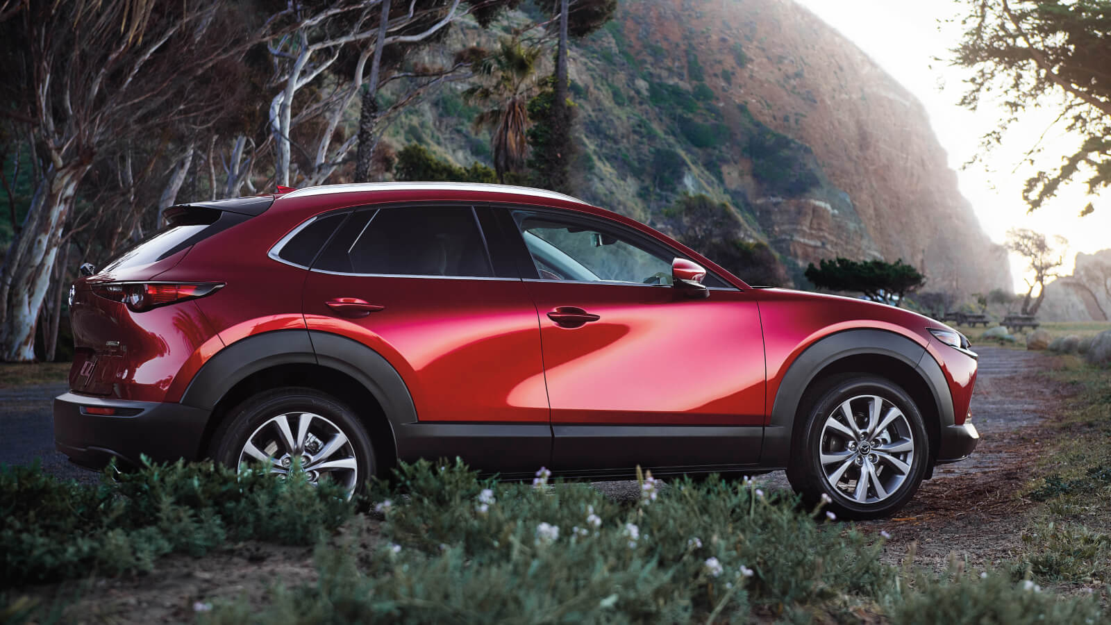 A red Mazda CX-30 driving on a dirt road nera a mountain.