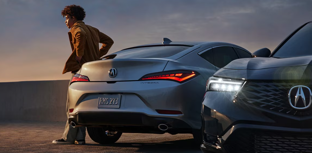 A man leans against a gray Acura Integra. A black Acura Integra is alongside the gray