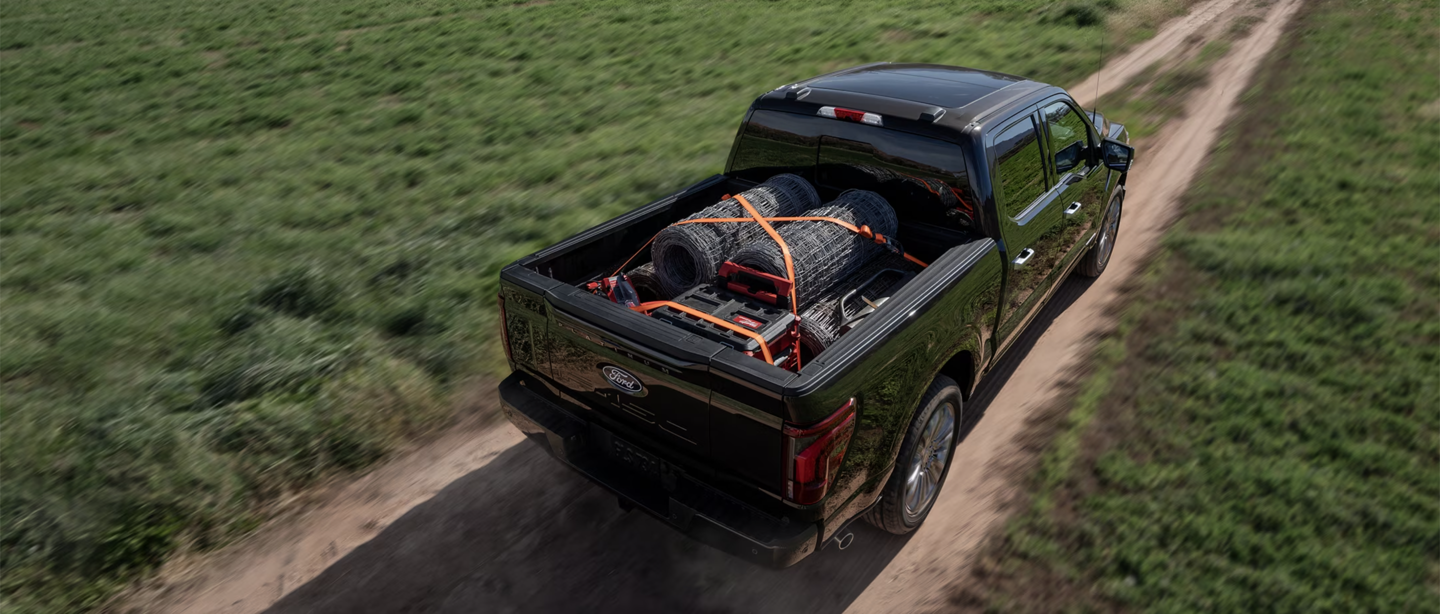 A rear overhead view of the 2024 Ford F-150 on a dirt road with materials strapped into the truck bed