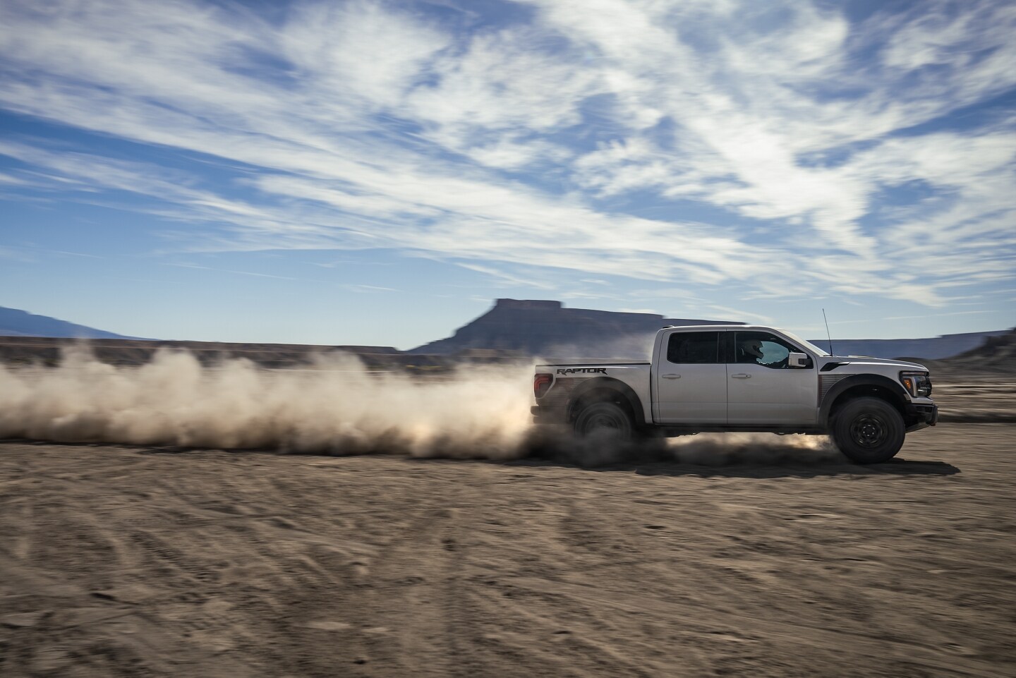 A white Ford F-150 driving in a desert and leaving a dirt trail behind it