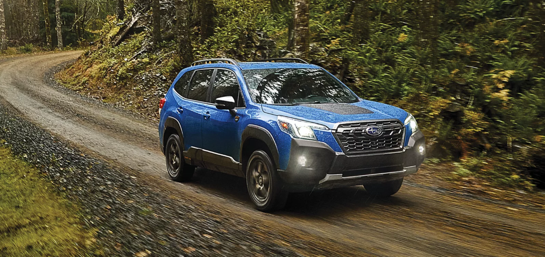 A blue 2024 Subaru Forester driving through a forest