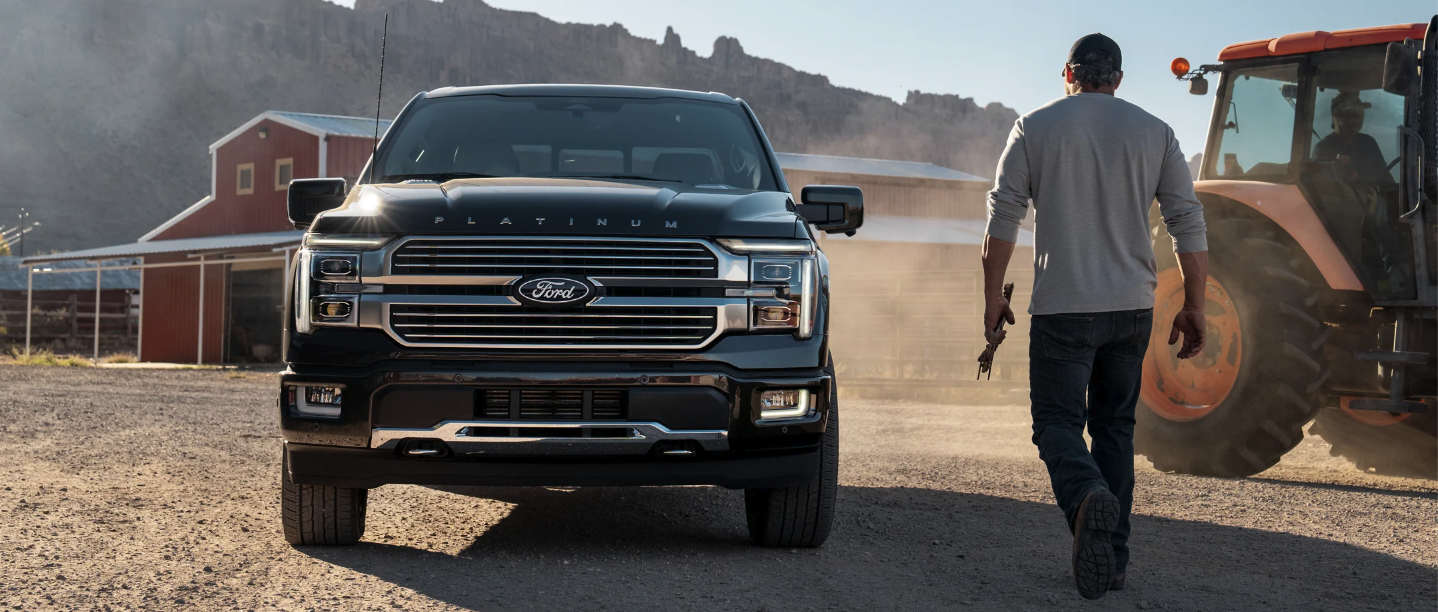A person walking toward a Ford hybrid vehicle next to a tractor