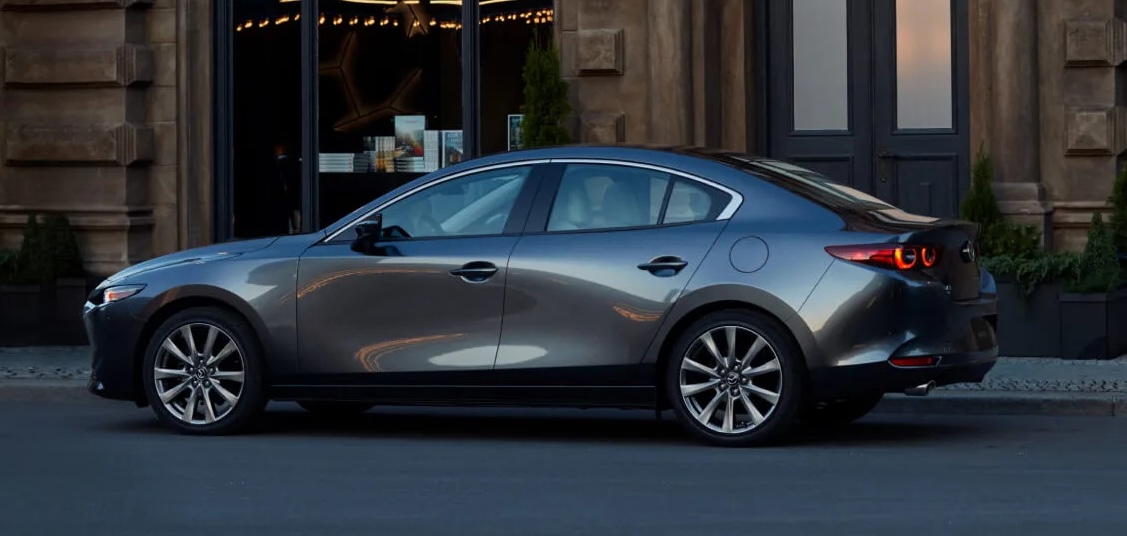 A gray Mazda3 sedan parked by the curb outside a building.
