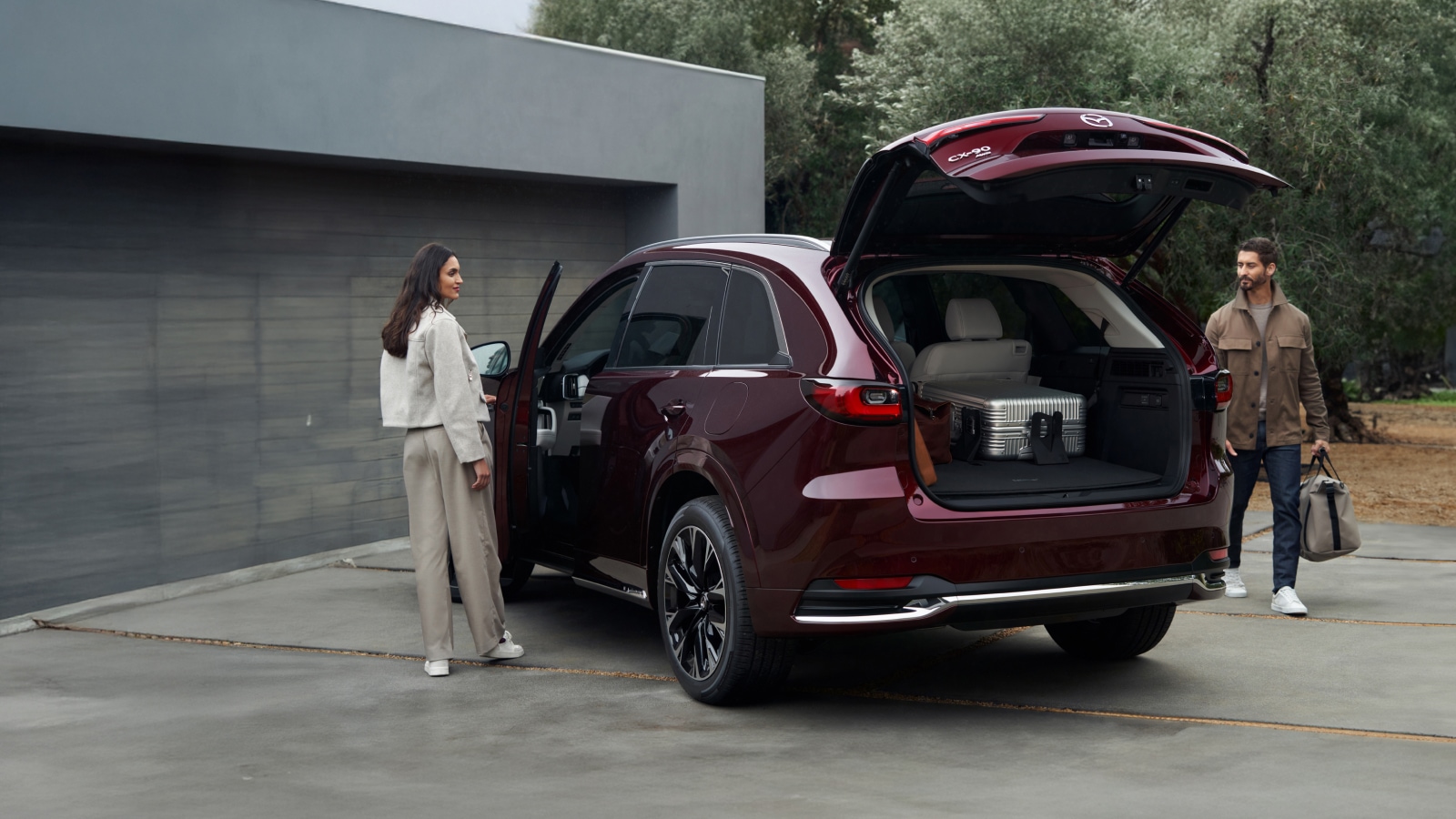 A burgundy Mazda CX-90 in a driveway being loaded up and entered by a couple
